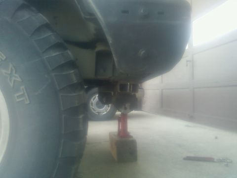 1988 Ford Bronco - A vehicle's rear bumper and tire are shown elevated on a jack, with another vehicle partially visible behind it.