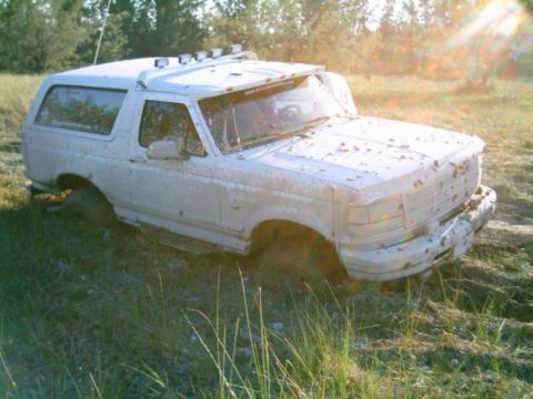 1995 Ford Bronco - A white SUV is stuck in the mud, with its front right tire deep in the mire.