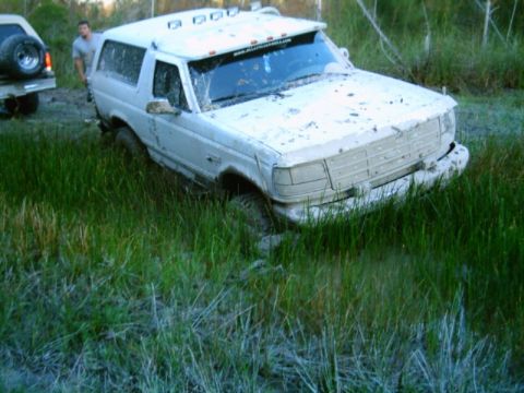 1995 Ford Bronco - A white 1995 Ford Bronco is stuck in the mud, with another vehicle visible in the background.