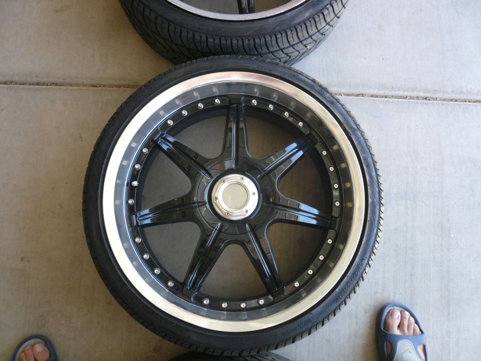 Black multi-spoke aftermarket wheel with polished lip and tire, viewed from above