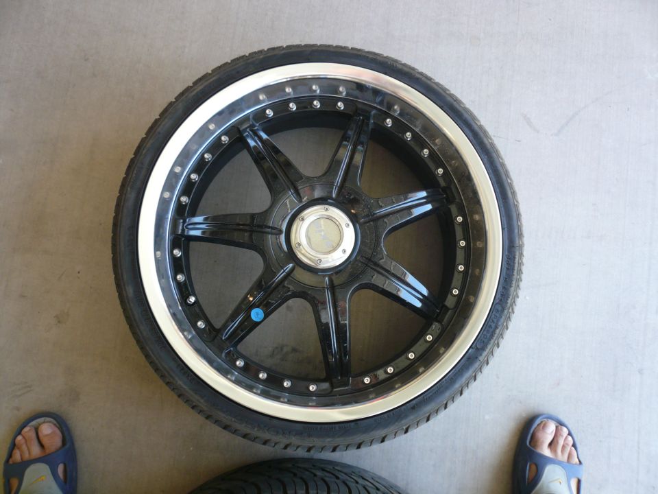 Black aftermarket wheel with chrome lip and tire, on concrete floor