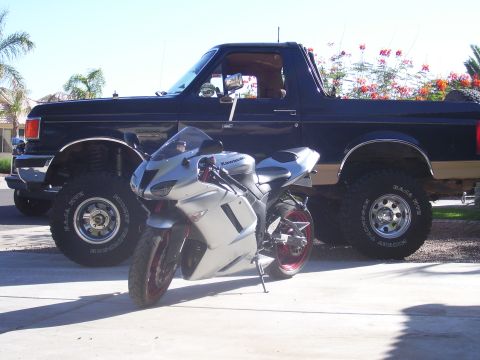1991 Ford Bronco - A silver sport motorcycle is parked in front of a black 1991 Ford Bronco.