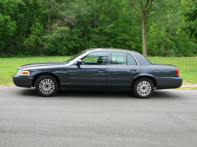 Side view of a dark gray sedan parked on a road with trees in the background
