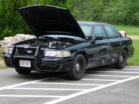 1997 Mercury Grand Marquis - A black police interceptor, possibly a Ford Crown Victoria, is parked with its hood open, revealing the engine compartment. The license pla…