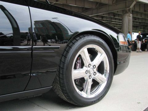 2003 Mercury Marauder - A black sedan is shown from the front quarter panel, focusing on the wheel and tire. Reflections show buildings and people.