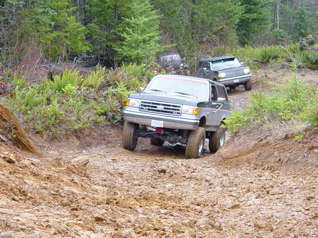 1992 Ford Bronco driving on a muddy off-road trail with another SUV behind it