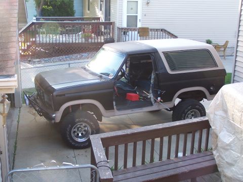1986 Ford Bronco - A two-tone brown and tan Ford Bronco is parked in a driveway with its doors open, showing tools and a red toolbox inside. The vehicle has a…