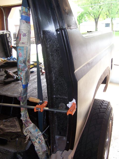 1986 Ford Bronco - A black textured surface on the interior of a vehicle's cab is being worked on, with orange clamps holding a metal bar in place. Newspaper…