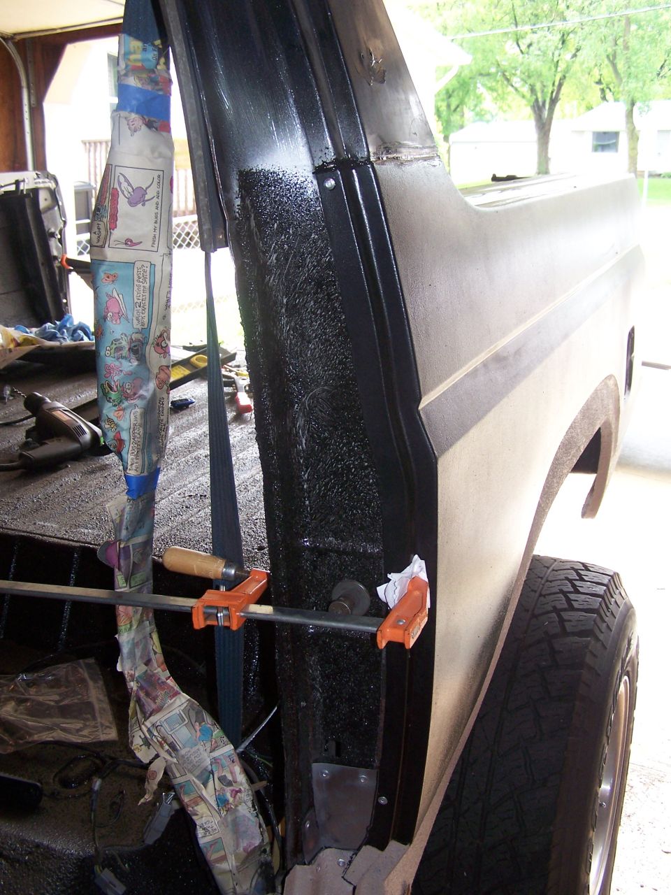 Close-up of a vehicle's black textured interior panel with orange clamps and newspaper.