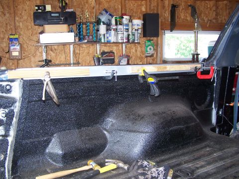 1986 Ford Bronco - The bed of a pickup truck is being worked on, with a spray-in bedliner applied. Several clamps and tools are visible, along with a wooden g…