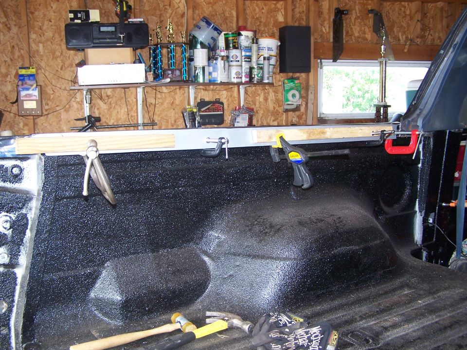 Pickup truck bed with spray-in liner, clamps, and tools.