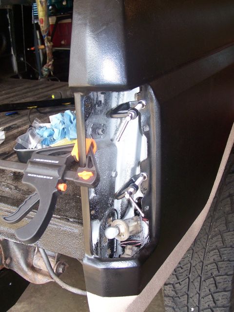 1986 Ford Bronco - A close-up view of the rear corner of a vehicle, showing a black taillight housing with exposed wiring and mounting hardware. A clamp is at…
