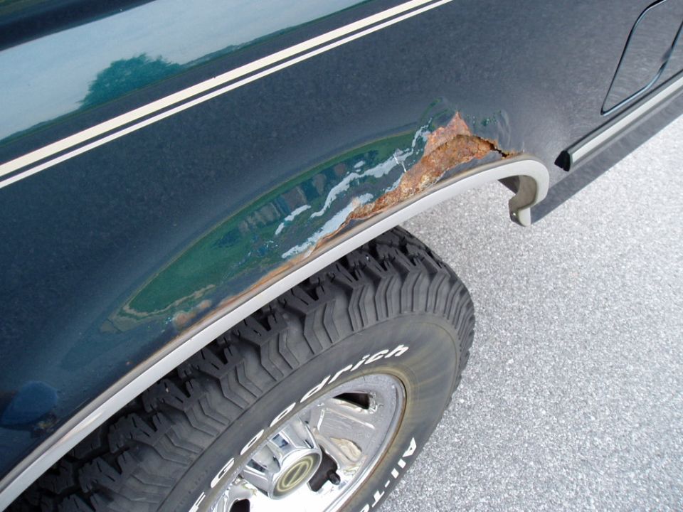 Close-up of rust on the rear fender of a dark green vehicle near the wheel well.