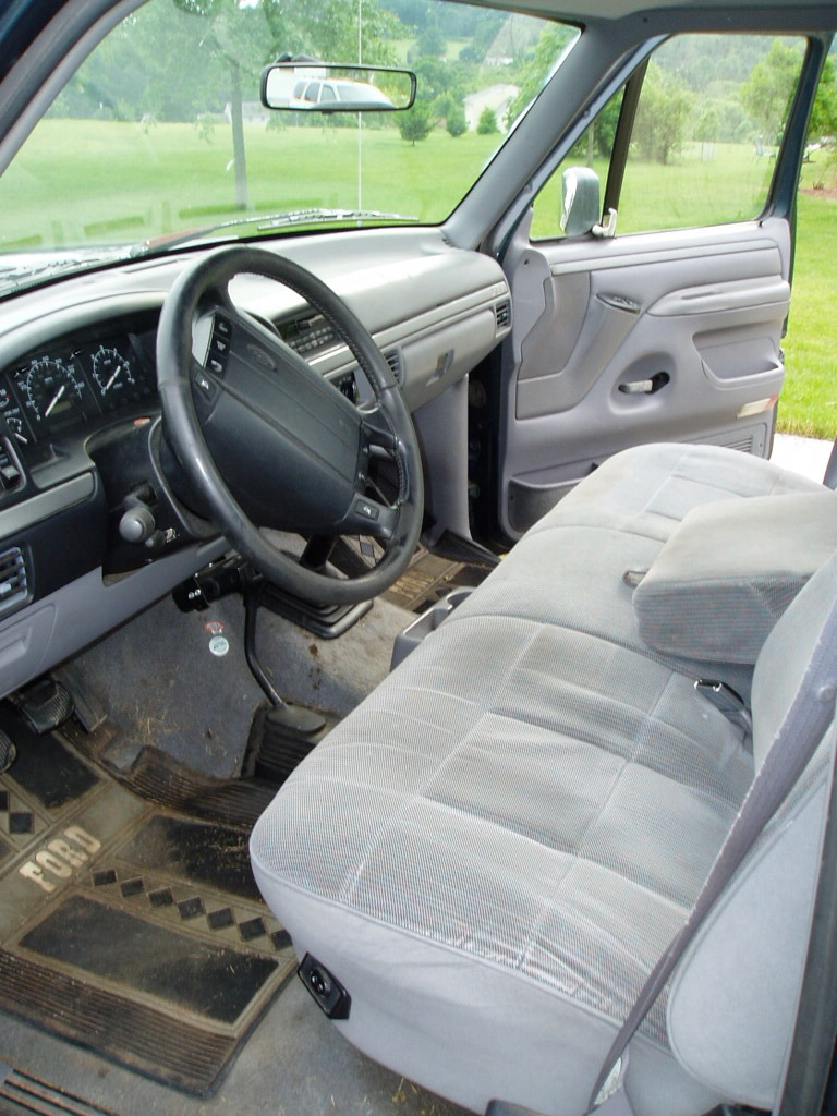 Grey cloth bench seat interior of a 1990s Ford pickup with manual shifter and Ford floor mats