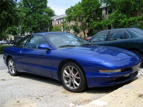 1993 Ford Probe - A blue 1993 Ford Probe is parked on a gravel driveway in front of apartment buildings.