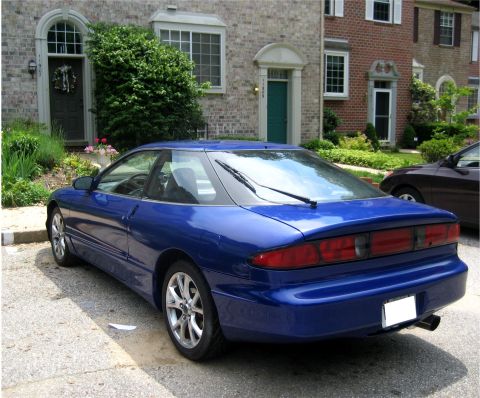 1993 Ford Probe - A blue 1993 Ford Probe is parked in front of a brick townhouse. The car is shown from a rear three-quarter angle, highlighting its coupe bo…