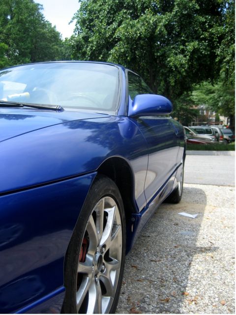 1993 Ford Probe - A low-angle, close-up shot of the driver's side of a blue 1993 Ford Probe. The car is parked on a gravel surface with trees in the backgrou…
