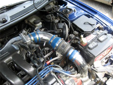 1993 Ford Probe - A close-up view of a modified engine bay, featuring a polished metal intake system with blue accents, a black engine cover, and a car batte…