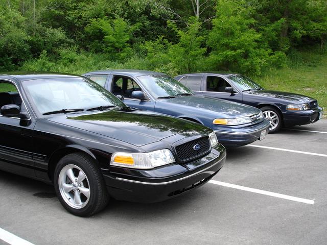 Three sedans parked in a lot, front-most is black, two behind are dark blue/gray.