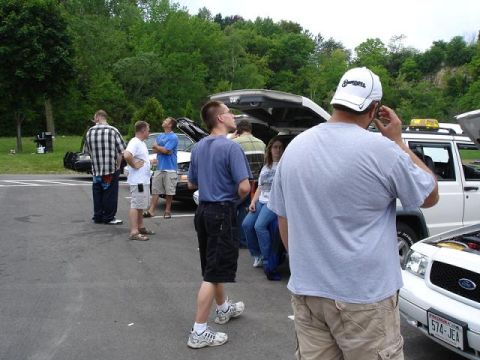 1997 Mercury Grand Marquis - A group of people stand around several vehicles, including a white Ford Crown Victoria with its hood open and a white SUV with its trunk op…