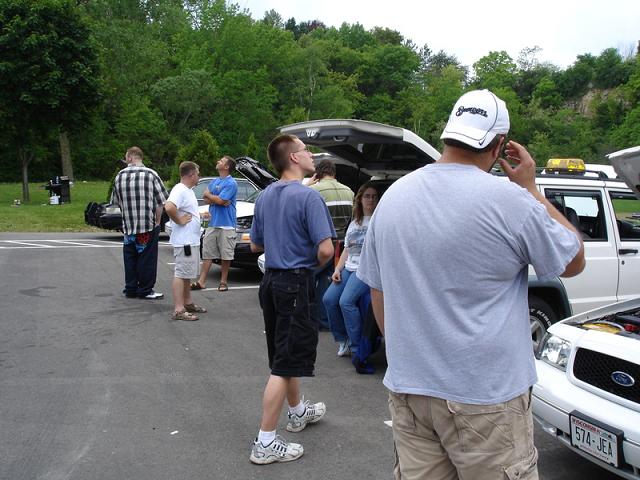 People gathered around cars, one with hood open, in a parking lot.