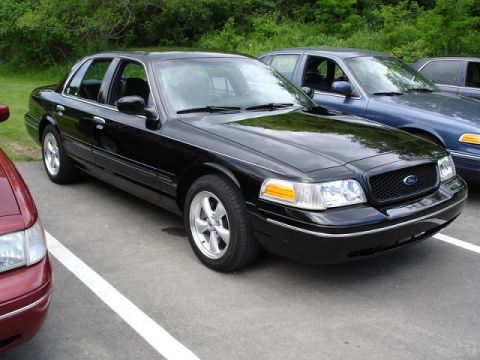 1997 Mercury Grand Marquis - A black four-door sedan is parked on a paved surface next to a blue sedan. The front of the black sedan is angled towards the viewer, showi…