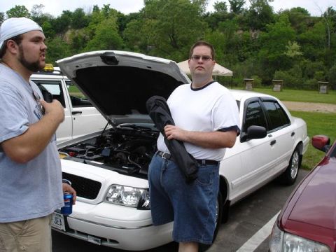 1997 Mercury Grand Marquis - Two men stand next to a white sedan with its hood open, revealing the engine. The car is parked outdoors on a paved surface with grass and…