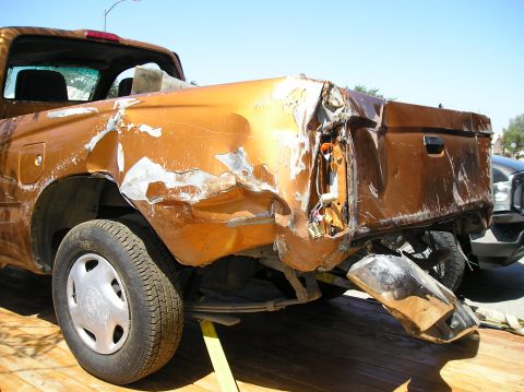 1986 Toyota Hilux - The rear passenger side of a heavily damaged orange pickup truck is shown, with significant body damage to the fender and tailgate area. Th…