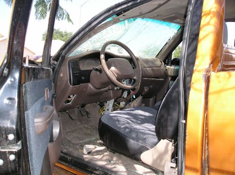 1986 Toyota Hilux - The interior of a damaged pickup truck shows a cracked windshield, a steering wheel, dashboard, pedals, and a driver's seat with visible wi…