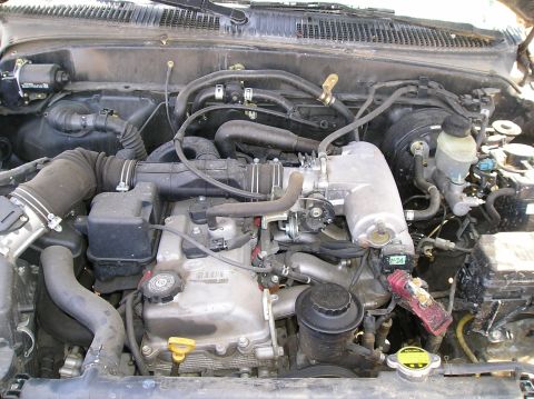 1986 Toyota Hilux - This is a close-up view of a dirty engine bay, likely from a Toyota Hilux, showing various hoses, the intake manifold, and engine component…