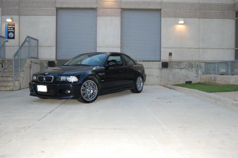 2002 BMW M3 - A black BMW M3 is parked in front of a commercial building with large roll-up doors.