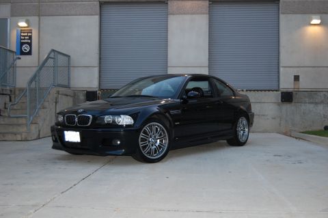 2002 BMW M3 - A black BMW coupe is parked in front of a building with closed garage doors.