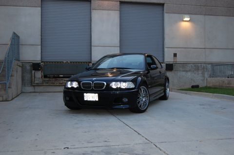 2002 BMW M3 - A black 2002 BMW M3 is parked in front of a loading dock, its headlights illuminated.