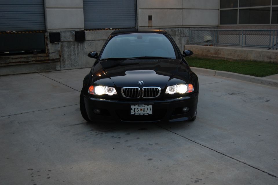 Black BMW M3 front view with headlights on.