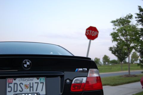 2002 BMW M3 - A black BMW M3 is parked near a stop sign with trees in the background.