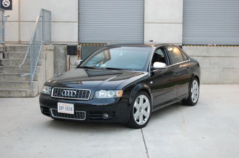 2002 BMW M3 - This black Audi sedan is parked in front of a building with large garage doors.