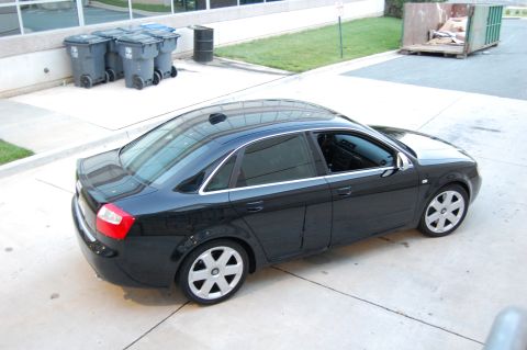 2002 BMW M3 - A black sedan is parked on a concrete surface with trash cans and a dumpster visible in the background.