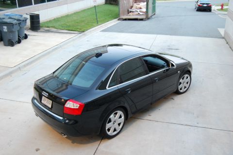 2002 BMW M3 - A black sedan is parked on a concrete surface, with trash bins and a dumpster visible in the background.