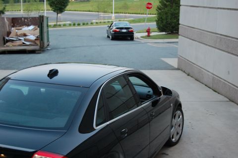 2002 BMW M3 - A black sedan is parked in a driveway, with another car driving away in the background near a stop sign.