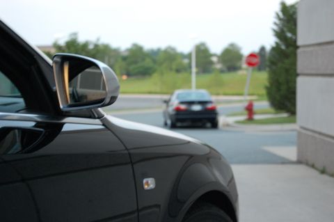 2002 BMW M3 - A black car is parked next to a building, with another car driving away in the distance.