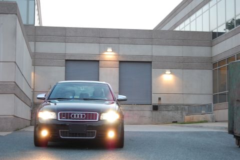 2002 BMW M3 - Front view of a black Audi S4 with its headlights on, parked outside a commercial building.