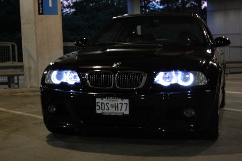 2002 BMW M3 - A black BMW sedan with distinctive halo headlights is captured from the front in a dimly lit parking structure.
