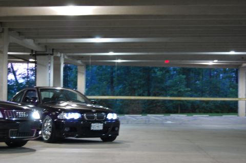 2002 BMW M3 - Two cars are parked in a dimly lit parking garage with trees visible in the background.