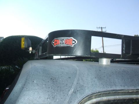 1988 Ford Bronco - Close-up of a roof rack with a prominent 'CON-FER-R' sticker and a yellow auxiliary light.