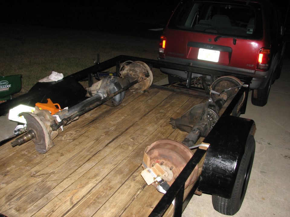Trailer loaded with two axles and a red SUV is hitched to it