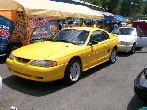 2001 Ford Mustang - A yellow Ford Mustang is parked at an outdoor event with other vehicles and tents in the background.