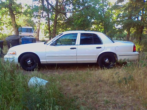 2000 Ford Crown Victoria - Side view of a white 2000 Ford Crown Victoria parked outdoors with trees and another vehicle in the background.