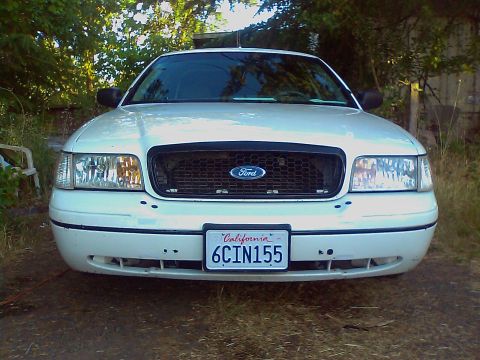 2000 Ford Crown Victoria - A white 2000 Ford Crown Victoria is parked outdoors with trees in the background.