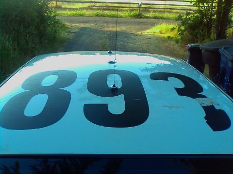 2000 Ford Crown Victoria - The top of a car shows large numbers and two antennas, with a dirt road and fence in the background.
