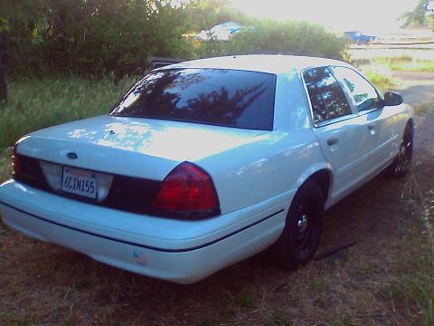 2000 Ford Crown Victoria - Rear view of a white 2000 Ford Crown Victoria sedan parked outdoors on a grassy area.